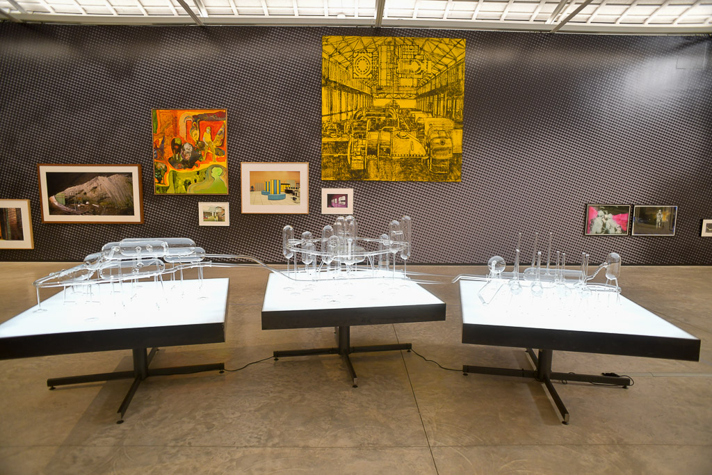 Ausstellungshalle mit Tischen und bunten Gemälden