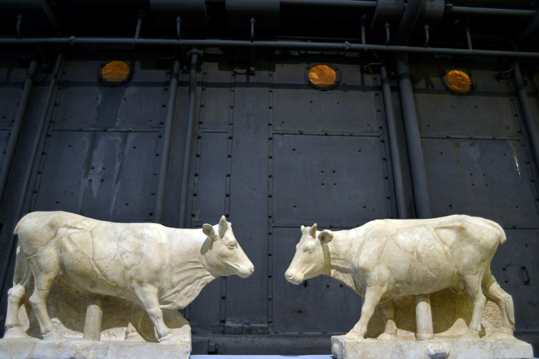 Zwei Stierfiguren vor einer Kesselwand