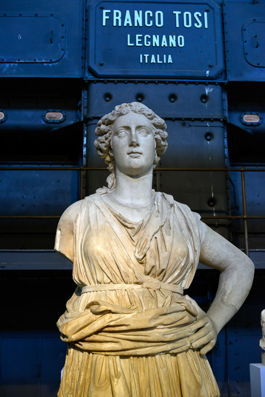 Frauenstatue vor einem Kessel im Hochformat
