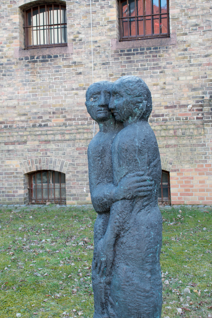 Skulptur vor Backsteinwand im Hochformat