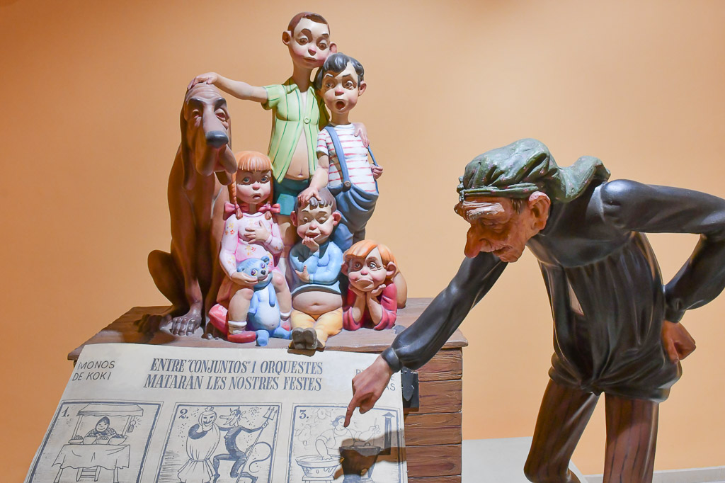 Figurengruppe mit Kindern und einem gebeugten Mann vor einer Zeitung