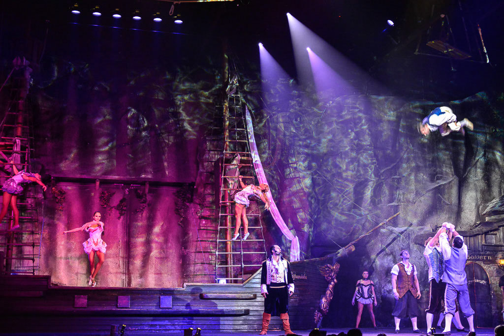 Show mit Lichtspots und einem Akrobaten in der Luft