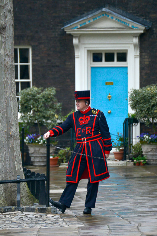 Yeoman Warder in blau-roter Uniform vor einem Haus im Hochformat