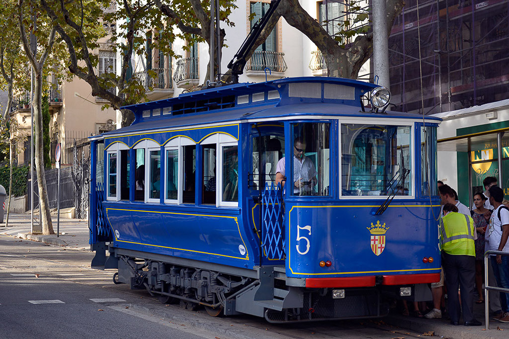 Blaue Straßenbahn mit Passanten am Straßenrand