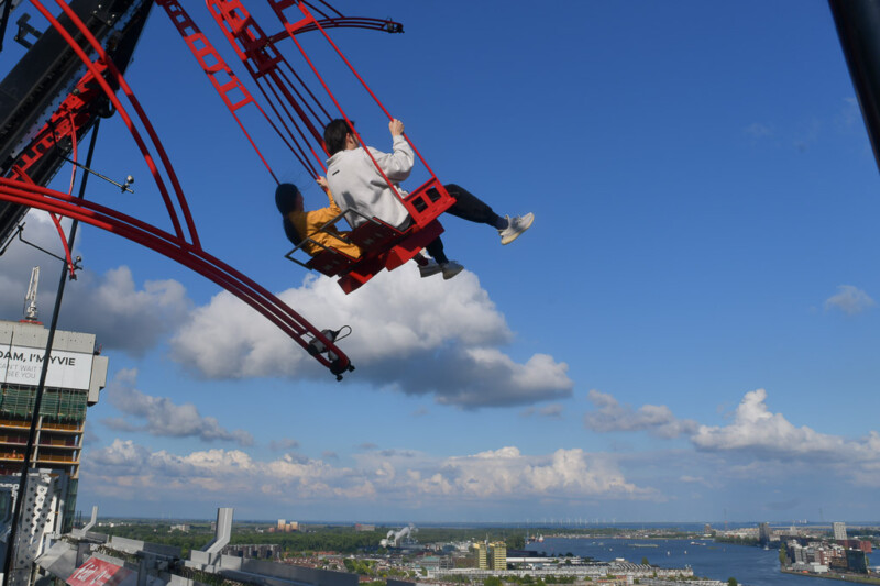 Schaukelnde Besucher vor blauem Himmel bei der Attraktion Over The Edge