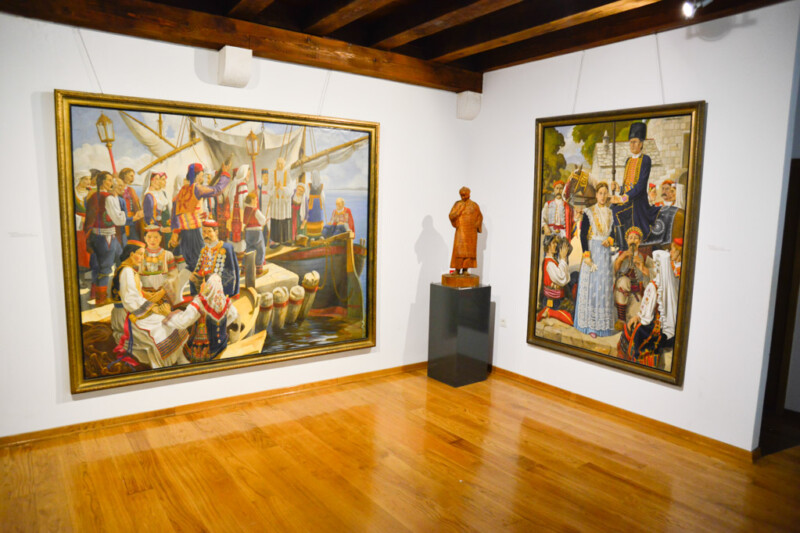 Großformatige Gemälde und eine Holzfigur im Ausstellungsraum