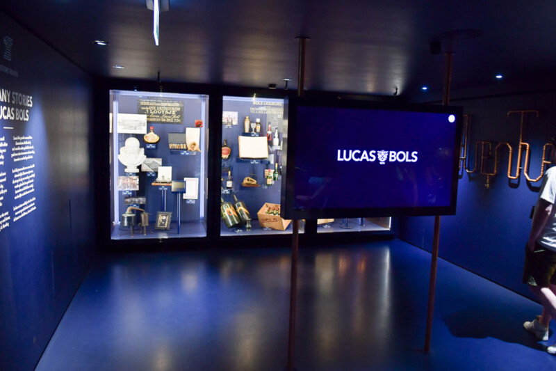 Dunkler Ausstellungsraum mit Vitrinen und Bildschirm im House of Bols