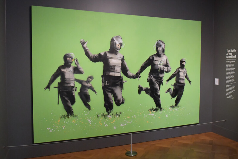 Banksy-Gemälde mit rennenden Figuren vor grünem Hintergrund im Moco Museum