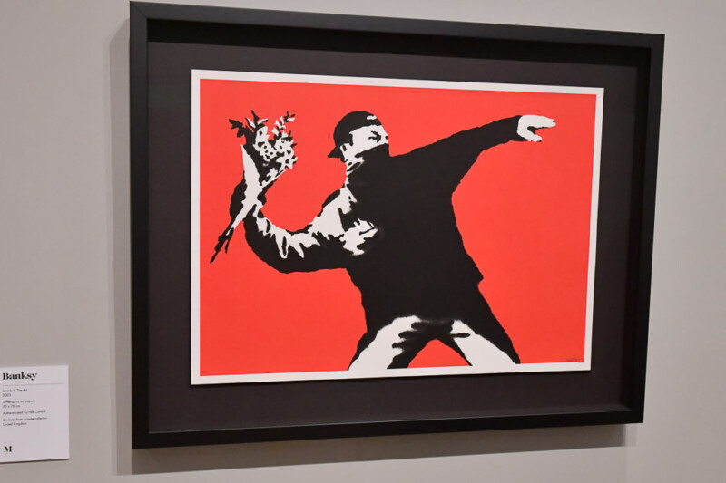 Banksys Werk Love is in the Air mit Blumenwerfer auf rotem Grund im Moco Museum