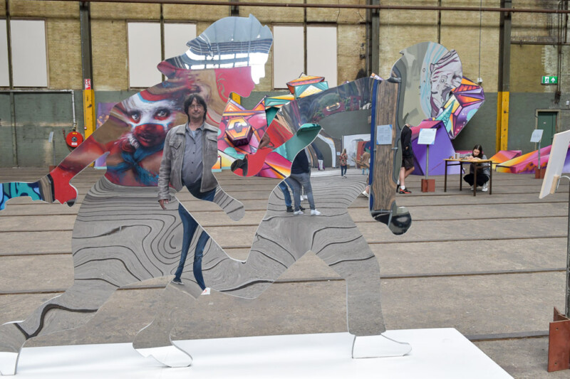 Skulpturen aus Metallplatten vor Wandbildern in der Halle